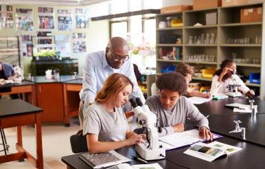 高中学生与导师在生物学上使用显微镜 